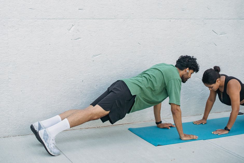 Man and woman practicing plank exercises outdoors on a yoga mat.