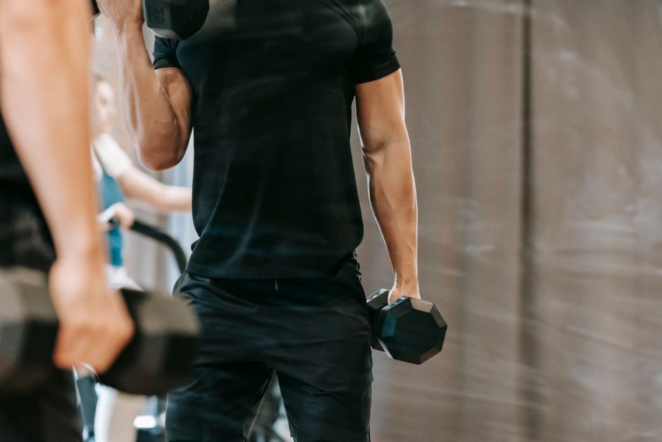 Unrecognizable muscular male u crnoj sportskoj opremi s bučicama u modernom fitness studiju