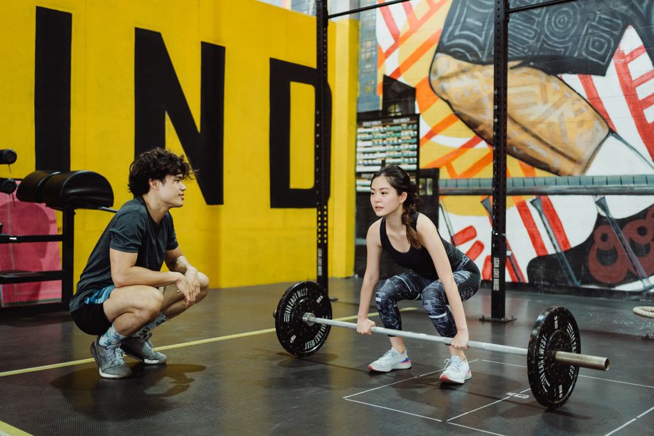 Young woman lifting weights guided by a trainer in a colorful gym setting.