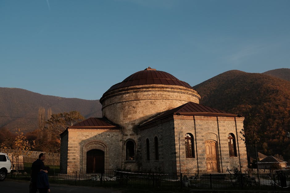 Majestic old stone building with a domed roof at sunset, set against mountain scenery